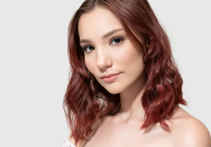 Portret młodej kobiety z falowanymi, mahoniowo-brązowymi włosami.
