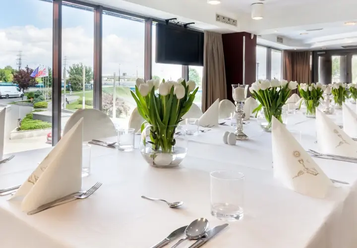 Elegancko nakryty stół z białymi tulipanami, idealny na uroczystość. Zastanawiasz się, ile trwa komunia w restauracji? To zależy od wielu czynników, ale zazwyczaj trwa kilka godzin.