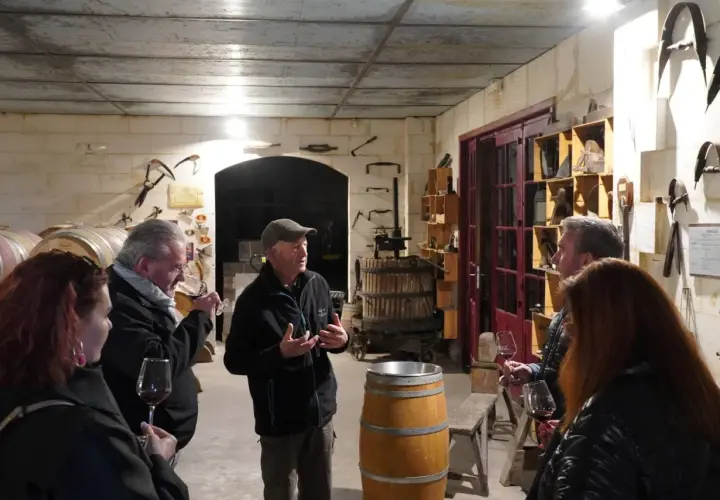 Visite d'une cave à vin du Médoc. Un guide explique la fabrication du vin à des visiteurs, entourés de fûts et d'outils anciens.