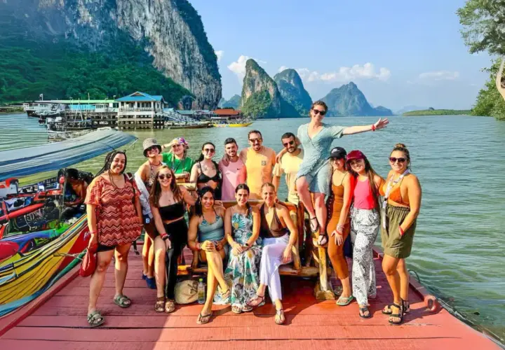 Grupo de amigos disfrutando en un barco en Tailandia, con islas kársticas al fondo. ¡Parece la mejor época para viajar a Tailandia!