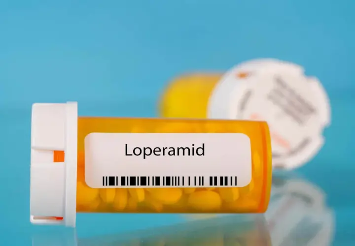 Orange pill bottle with "Loperamid" label and yellow pills inside. Another blurred bottle in the background.