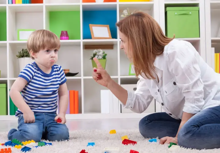 Niño con cara de enfado, actitud negativista desafiante, mientras su madre le regaña.