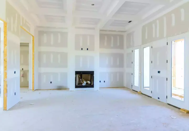 Interno di una casa in costruzione, con pareti e soffitto in cartongesso, camino e porte finestre.