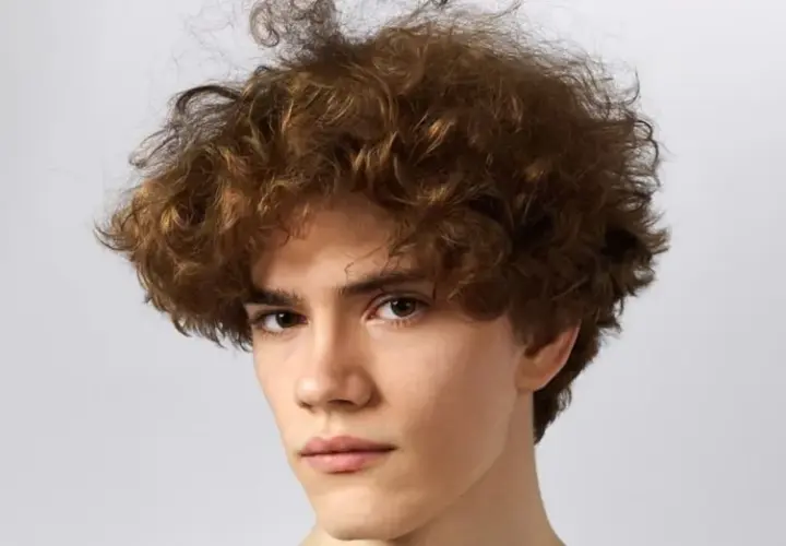 Joven con pelo castaño rizado y voluminoso, un estilo moderno que realza sus rasgos. Cortes pelo rizado hombre.