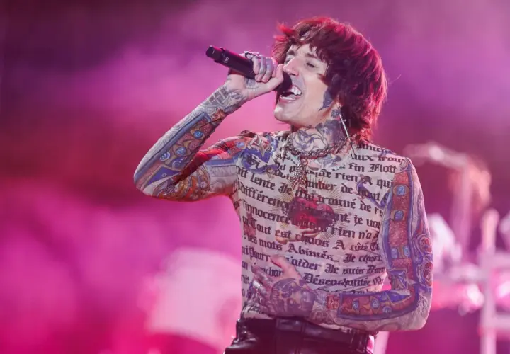 Oli Sykes z Bring Me The Horizon Polska śpiewa na koncercie, ubrany w koszulkę z tatuażami i francuskim tekstem.