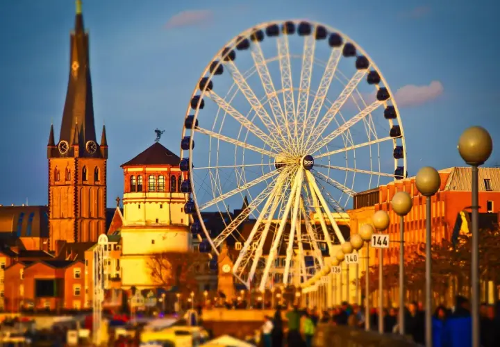Zachód słońca nad Renem, gdzie dusseldorf atrakcje, takie jak diabelski młyn i wieża kościelna, tworzą malowniczy krajobraz.