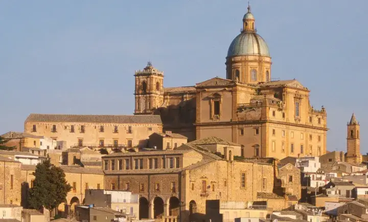 Vue panoramique de la ville de Piazza Armerina en Sicile, dominée par une imposante cathédrale à dôme vert.