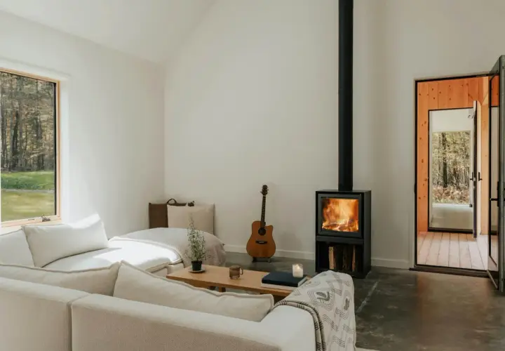 Salon cosy avec poêle à bois allumé, guitare et canapé. Une aide financière pour le tubage de cheminée pourrait rendre ce lieu encore plus chaleureux.