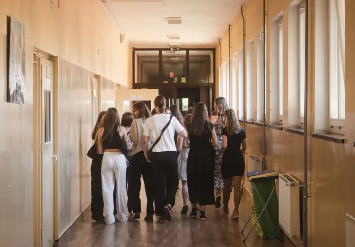 Grupa uczniów w szkolnym korytarzu, nerwowo oczekująca na rozpoczęcie egzaminów ósmoklasisty.