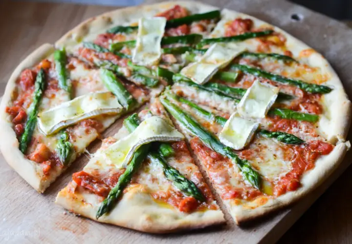 Pyszna pizza ze szparagami i serem brie, pokrojona na kawałki, prezentuje się apetycznie na drewnianej desce.