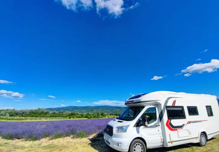 Un camping-car blanc stationné devant un champ de lavande en fleur, sous un ciel bleu éclatant en Provence.