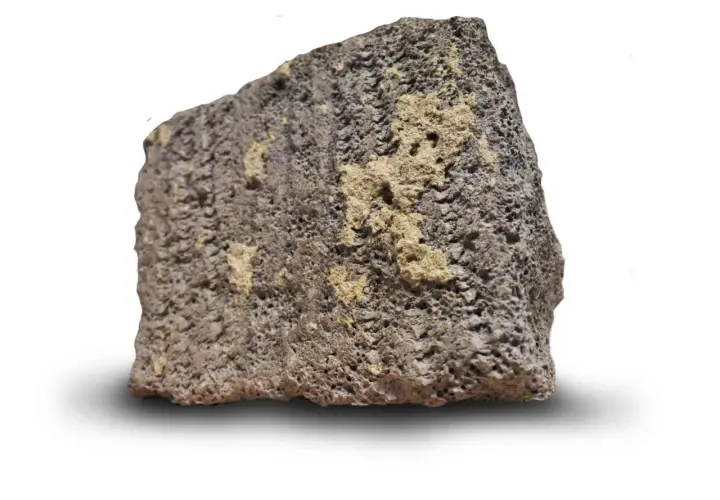 Ett stycke porös sten med mörkgrå och gulaktiga partier. Dess blåbetong utseende ger en känsla av naturlig textur.