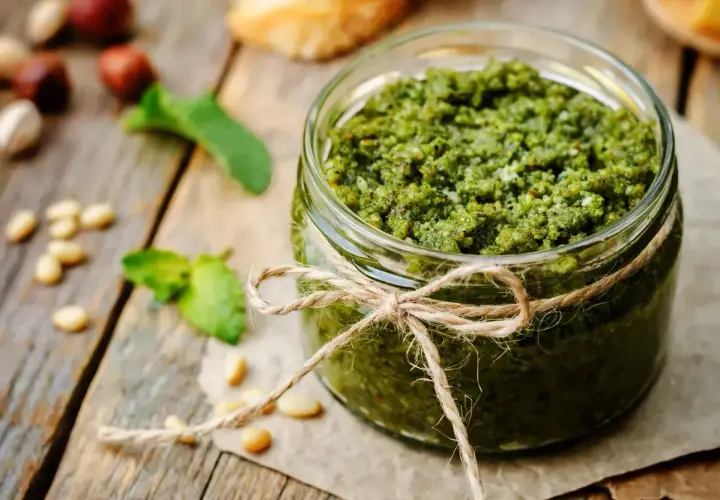 Słoik domowego pesto, ozdobiony sznurkiem, z orzeszkami pinii i listkami bazylii. Idealny przepis, jak zrobić pesto.