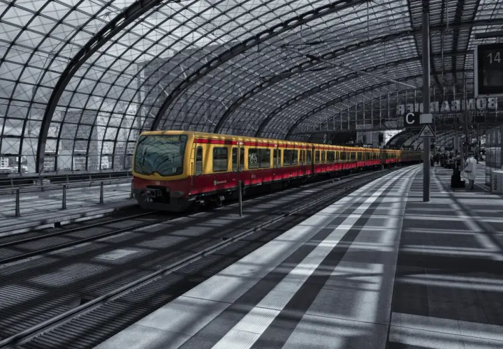 Żółto-czerwony pociąg S-Bahn Berlin stoi na nowoczesnym, zadaszonym peronie.