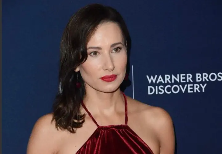 Aleksandra Popławska w bordowej sukni, znana z wielu filmów, seriali i programów, pozuje na tle logo Warner Bros. Discovery.