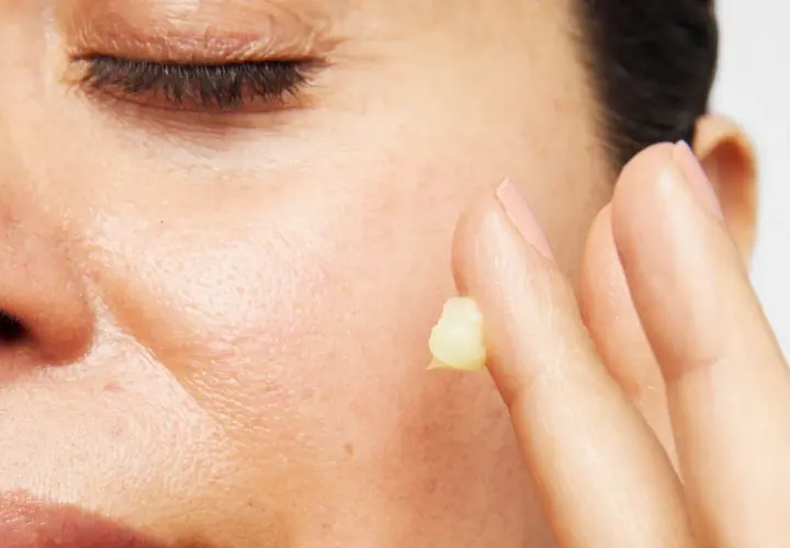 Närbild på en persons ansikte med slutna ögon. Ett finger med en klick kräm, kanske för att visa retinol resultat.