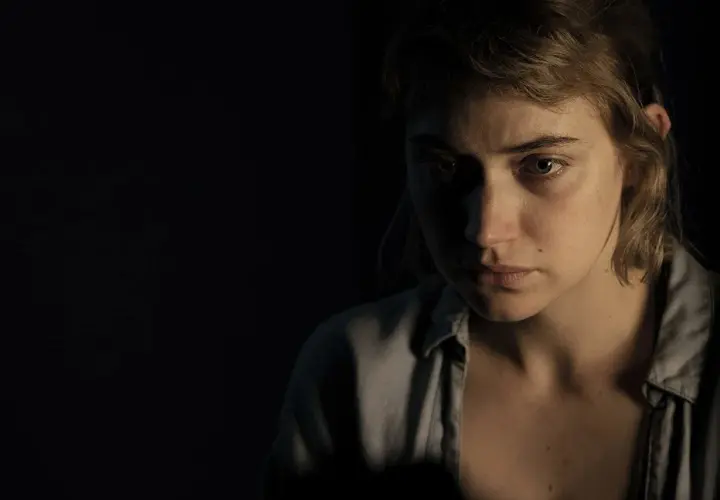 Primo piano di una giovane donna con sguardo preoccupato, in penombra. Un'immagine che evoca le atmosfere di "Vivarium", recensione.