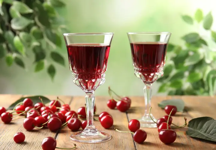 Dwa kieliszki z rubinowym alkoholem z wiśni, otoczone świeżymi owocami i zielonymi liśćmi.