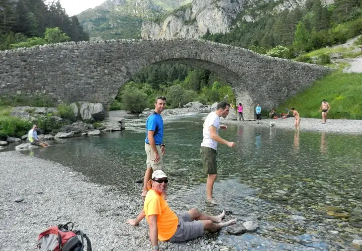 Gente disfrutando del río bajo el puente de piedra en Bujaruelo, con vistas al Taillón.