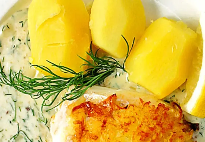 En gyllene fiskbit med krämig dillsås till fisk, serverad med kokt potatis och en citronskiva.