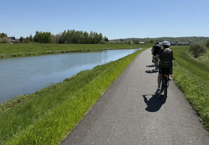 Rodzina na rowerach wzdłuż kanału. Słoneczny dzień sprzyja rodzinnemu **velo skawa** pośród zielonych łąk i drzew.