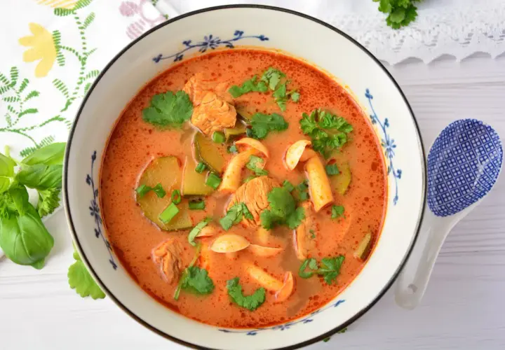 Aromaticzna zupa tom yum z kurczakiem, grzybami i kolendrą w misce z niebieskim wzorem. Obok leży łyżka.