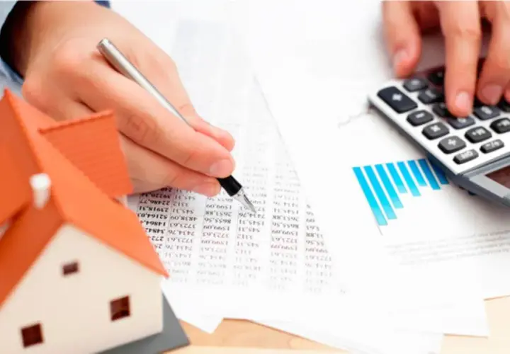 Manos calculando el tasador de casas precio con calculadora y modelo de casa.