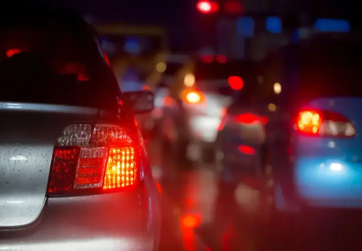 Czerwone światła stopu, czyli "brems licht co to znaczy", oznaczają hamowanie. Samochody stoją w korku nocą, ich światła odbijają się na mokrej drodze.