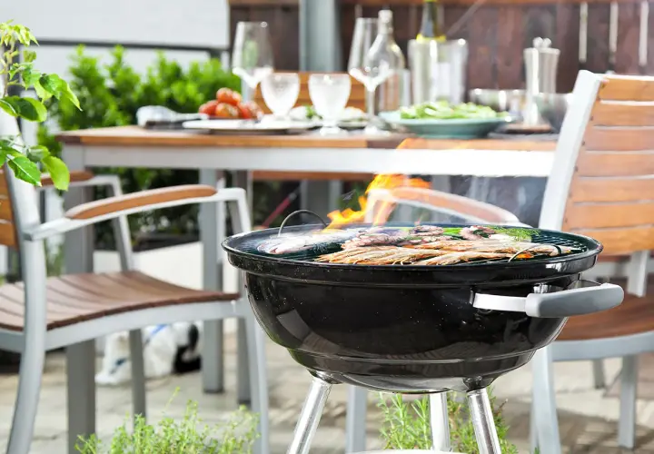 Un barbecue est allumé, des crevettes et du poisson grillent sur la grille. La table est dressée pour un repas en plein air.