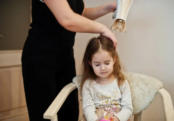 Mama suszy włosy córki suszarką, dbając o delikatną pielęgnację włosów dziecka.