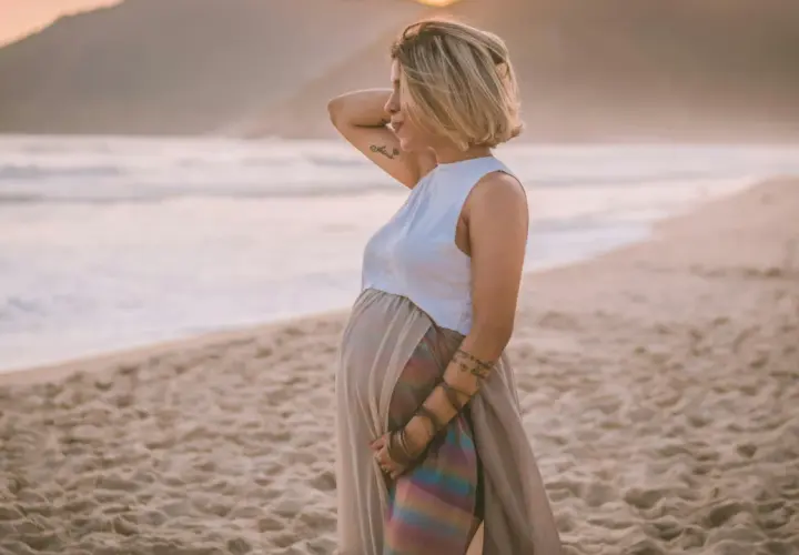 Donna incinta in piedi sulla spiaggia al tramonto, con il mare sullo sfondo. Un momento di pace e attesa, un vero mare in gravidanza.