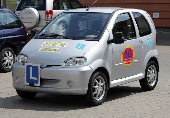 Srebrny czterokołowiec z literą "L" na masce i z boku, gotowy do nauki jazdy.