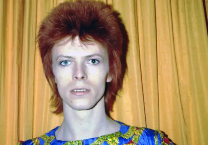Ikoniczny David Bowie z burzą rudych włosów i niebieskimi oczami, w stroju przypominającym jego słynne kreacje. Jego muzyka, jak te utwory, wciąż inspiruje.