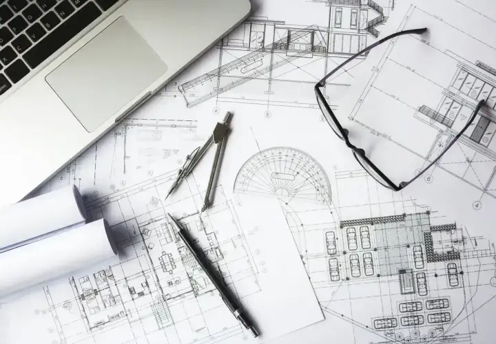 Na stole leżą plany architektoniczne, laptop, cyrkiel, linijka i okulary. To idealne miejsce do pracy nad kosztorysem budowlanym wzór.