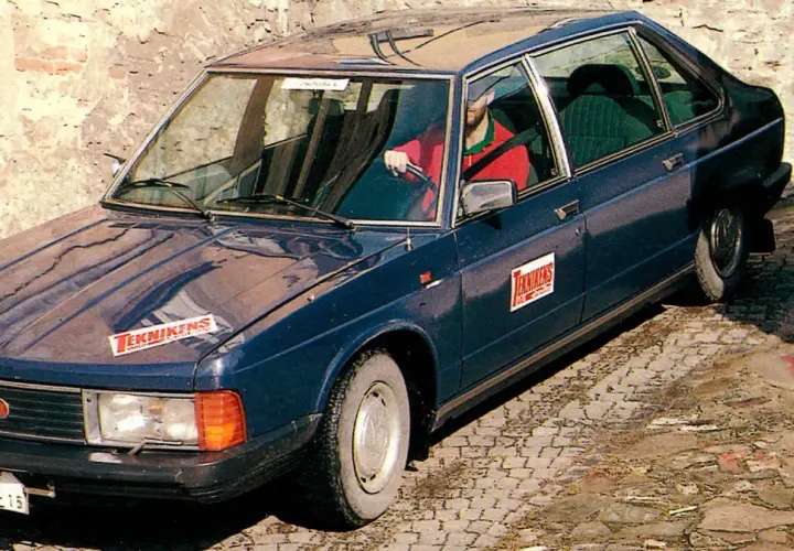 Mörkblå tatra bil med "Teknikens Värld"-logga på huven och dörren. En man i röd tröja kör.