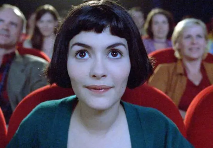 Amelia z uśmiechem na twarzy ogląda filmy podnoszące na duchu w kinie, otoczona innymi widzami.
