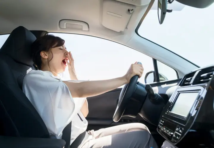 Mujer bostezando al volante, indicando que circunstancias del entorno favorecen la aparición de fatiga, como un viaje largo o la falta de sueño.