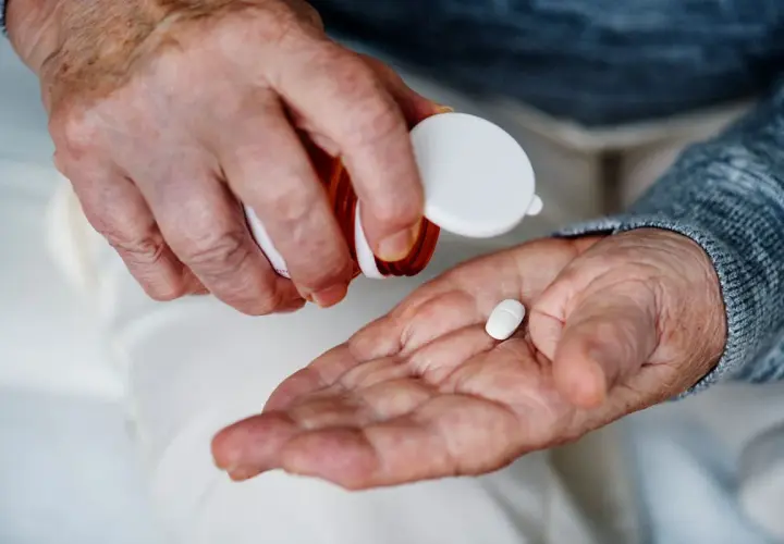 Manos de anciano vertiendo una pastilla blanca en su palma para tomar magnesio.