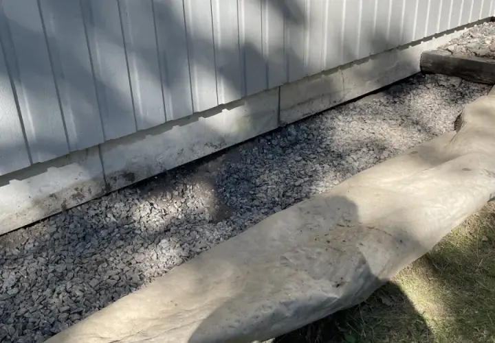 Grå makadam fyller utrymmet under husets grund, en del av arbetet med att bestämma hur mycket makadam under platta som behövs för dränering.