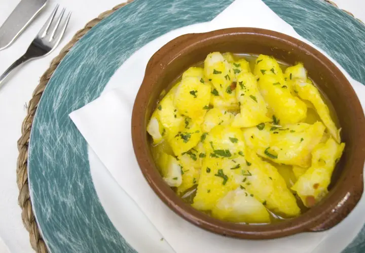 Delicioso bacalao a la cazuela, con trozos tiernos de pescado en una salsa dorada y perejil picado, servido en una cazuela de barro.