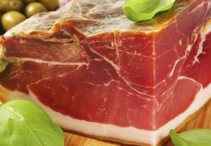 Ein Block Parma-Schinken, mariniert mit Kräutern, daneben grüne Oliven. Was ist Parmaschinken? Ein Genuss!