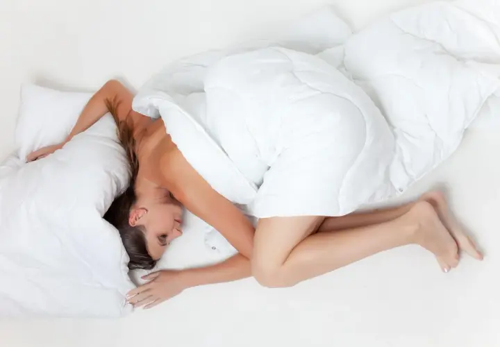 En andfådd gravid kvinna sover på sidan, insvept i ett vitt täcke.