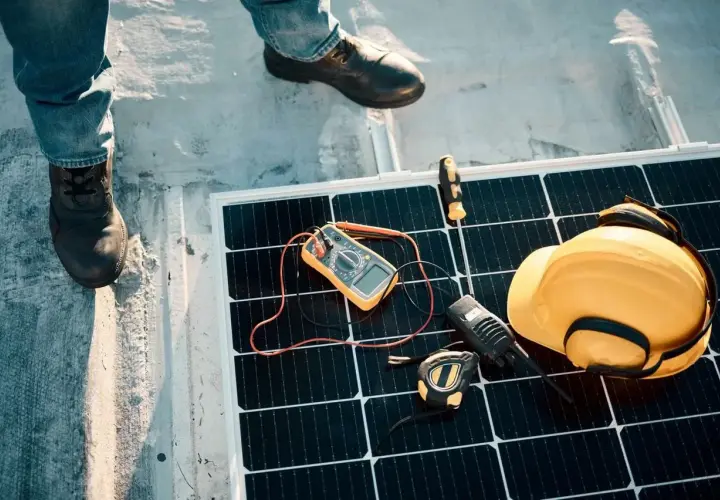 Instalatorzy sprawdzają panel słoneczny. Na panelu leżą miernik, żółty kask, krótkofalówka i taśma miernicza. Zabezpieczenie przeciwprzepięciowe jest kluczowe.