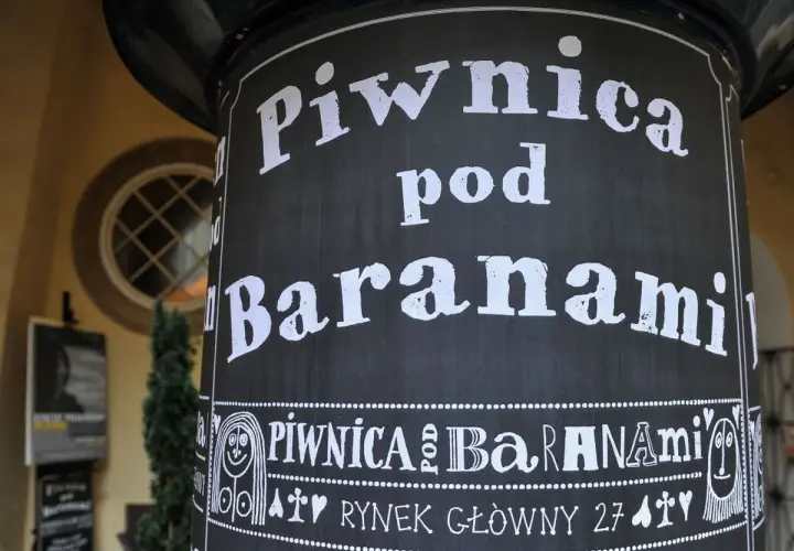 Czarny słup z białym napisem "Piwnica pod Baranami" i ozdobnymi elementami.