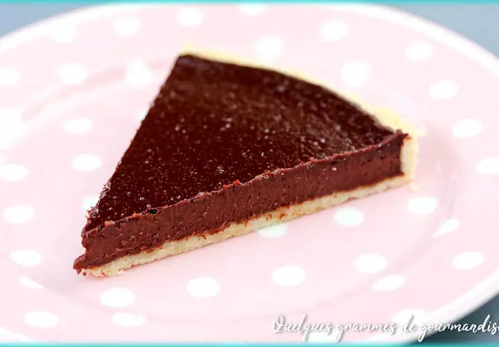 Une part de tarte au chocolat facile, avec une garniture riche et une pâte croustillante, servie sur une assiette rose à pois blancs.