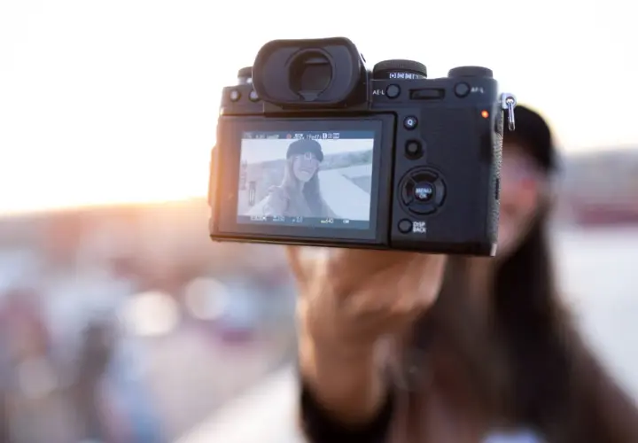 Aparat fotograficzny trzymany przez rękę, na ekranie selfie uśmiechniętej kobiety.