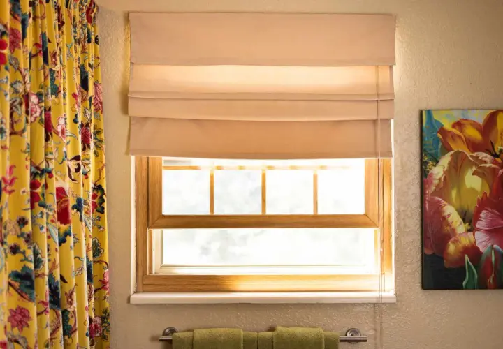 A beige Roman shade is partially lowered over a window, showing how to make Roman shades with its neat folds.