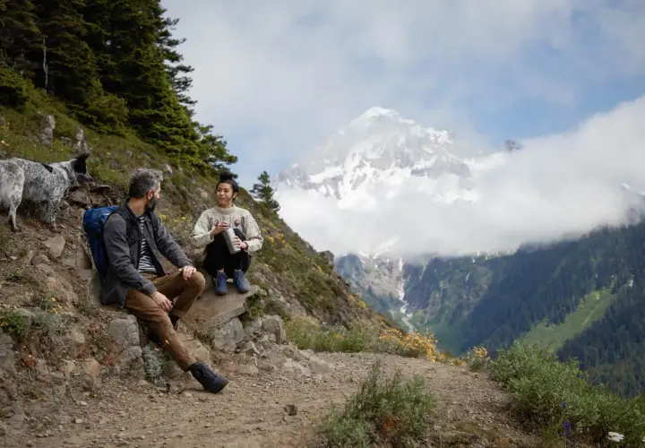 Para, pies i pies odpoczywają na szlaku, podziwiając majestatyczne góry. To właśnie jest **trekking co to** – przygoda i bliskość natury.