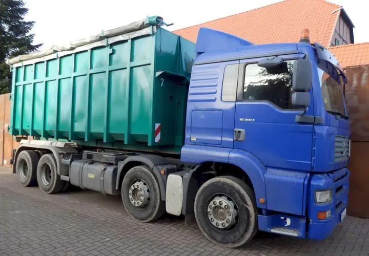 Blauer LKW mit großem grünen Container. Die Bedeutung eines solchen LKW ist der Transport von Schüttgut oder Abfall.