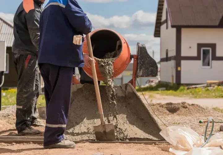 Dwóch budowlańców pracuje przy betoniarce. Wylewa się z niej świeży beton. Pytanie: ile cementu na betoniarkę 200?
